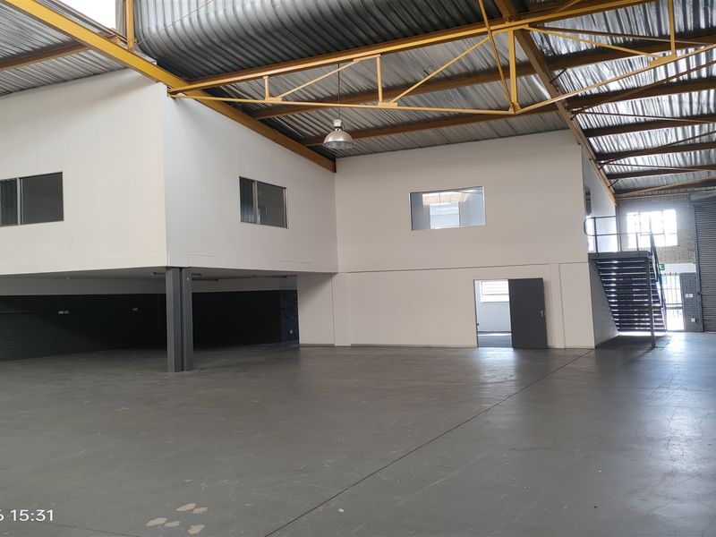 Spacious industrial warehouse unit featuring a mezzanine level, high-clearance steel roof trusses, concrete flooring, and a large roller shutter door for easy access.