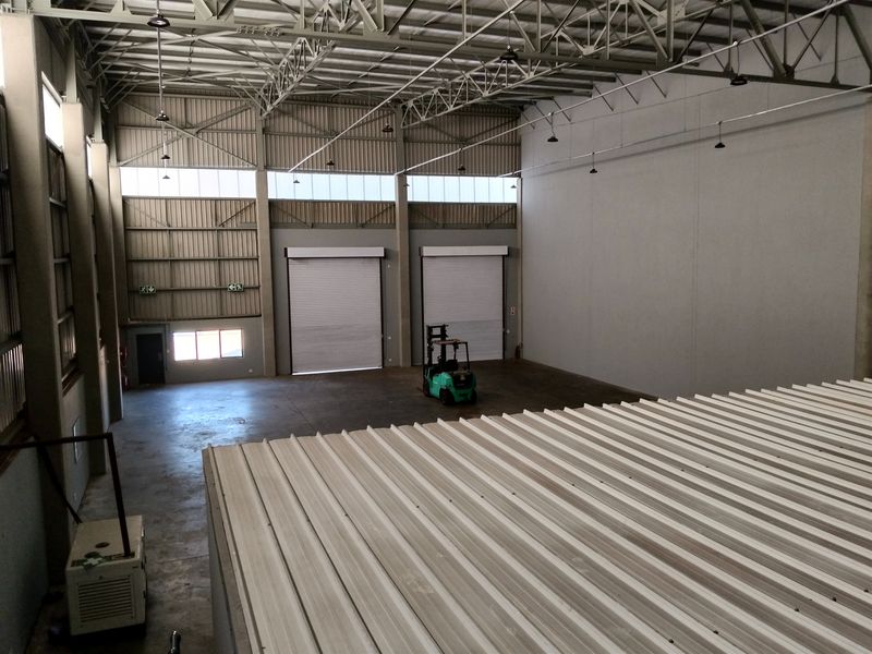 Spacious industrial warehouse featuring high ceilings with exposed steel trusses, concrete flooring, and dual roller shutter doors for efficient access.