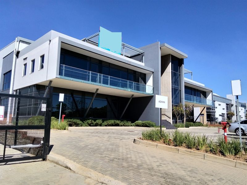 Modern industrial office building featuring a contemporary glass and concrete facade, paved driveway, and secure perimeter fencing.