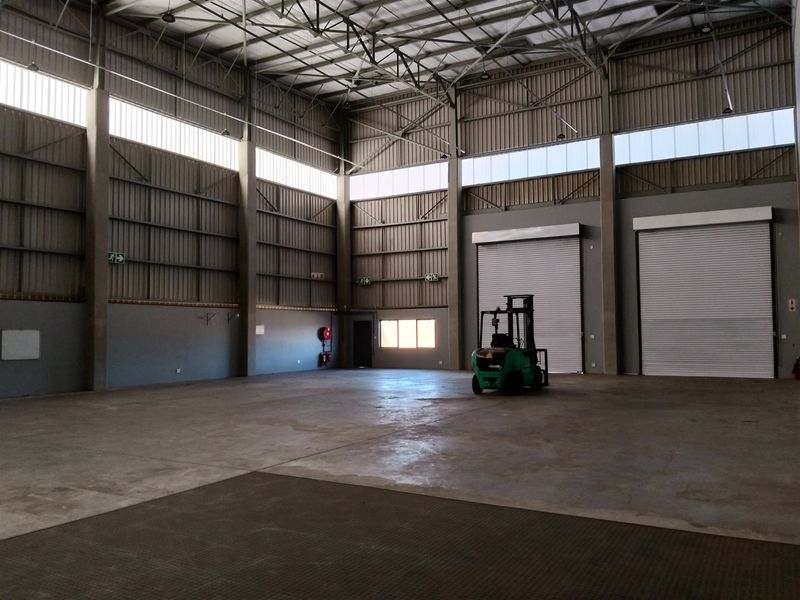 Spacious industrial warehouse featuring high ceilings with exposed steel trusses, concrete flooring, and multiple large roller shutter doors for efficient access.