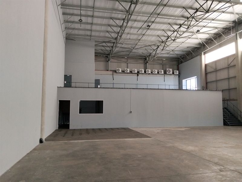Spacious industrial warehouse unit featuring high ceilings with exposed steel trusses, a mezzanine level, concrete flooring, and multiple wall-mounted air conditioning units.