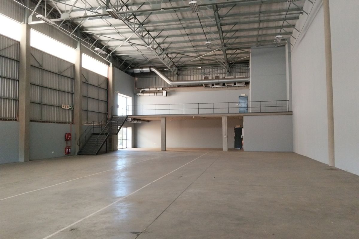 Spacious industrial warehouse unit featuring high ceilings with exposed steel trusses, a mezzanine level, concrete flooring, and integrated ventilation ducting.