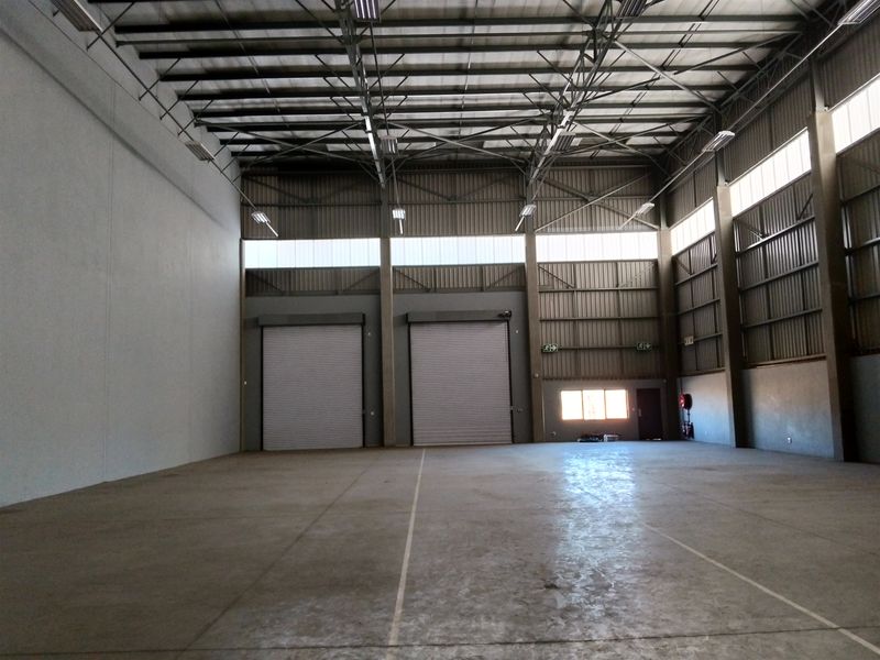 Spacious industrial warehouse unit featuring high-volume ceilings, exposed steel trusses, concrete flooring, and dual roller shutter doors for efficient access.