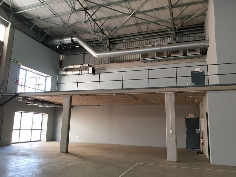 Spacious industrial unit featuring a mezzanine level, exposed steel roof structure, HVAC ducting, and large windows providing ample natural light.
