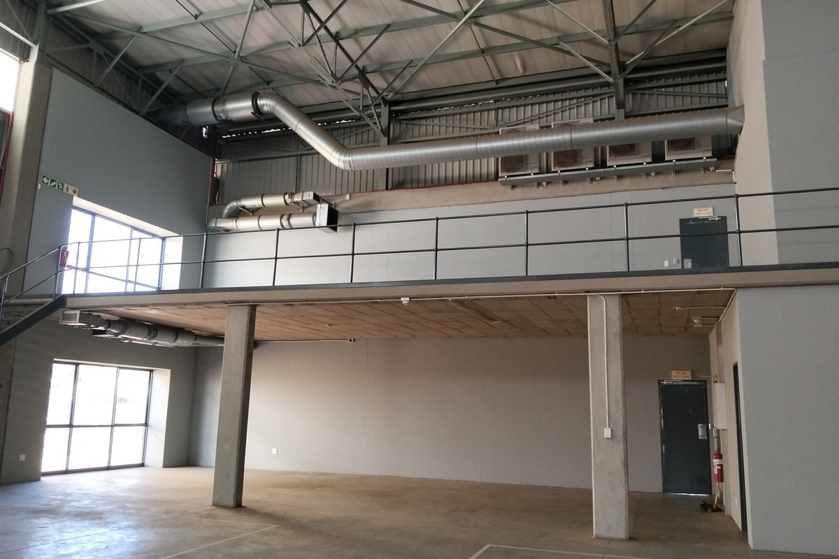 Spacious industrial unit featuring a mezzanine level, exposed steel roof structure, HVAC ducting, and large windows providing ample natural light.