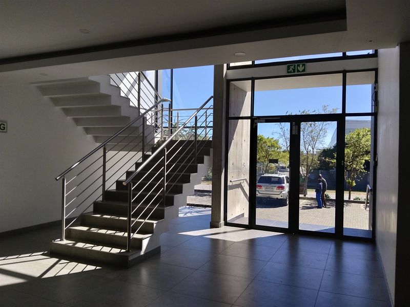Modern industrial-style entrance lobby featuring a prominent staircase with stainless steel balustrades, large glass doors, and polished floor tiles.
