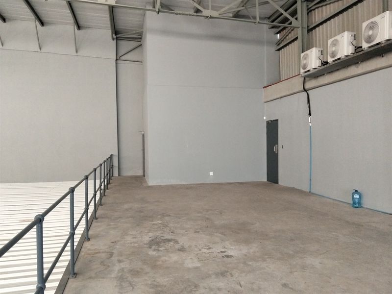 An open-plan industrial mezzanine area featuring exposed steel roof trusses, concrete flooring, and wall-mounted air conditioning units.