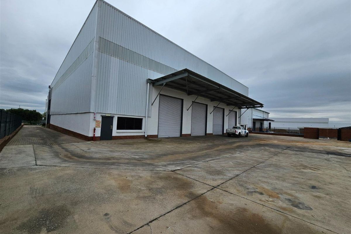 Industrial warehouse exterior featuring multiple roller shutter doors, a loading canopy, and a large concrete yard area.