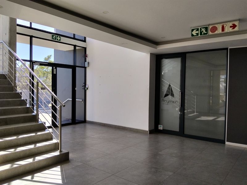 Modern industrial entrance lobby featuring tiled flooring, a staircase with stainless steel handrails, and glass-paneled doors providing natural light.