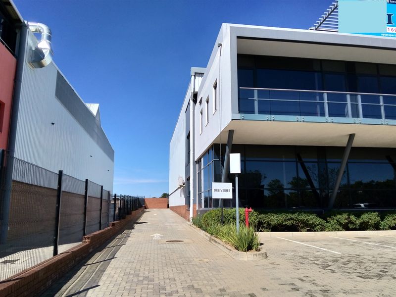 Exterior view of the industrial property showing a paved delivery access driveway, modern glass facade, and balcony area.