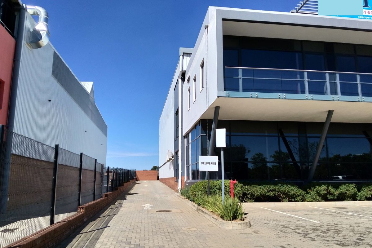 Exterior view of the industrial property showing a paved delivery access driveway, modern glass facade, and balcony area.