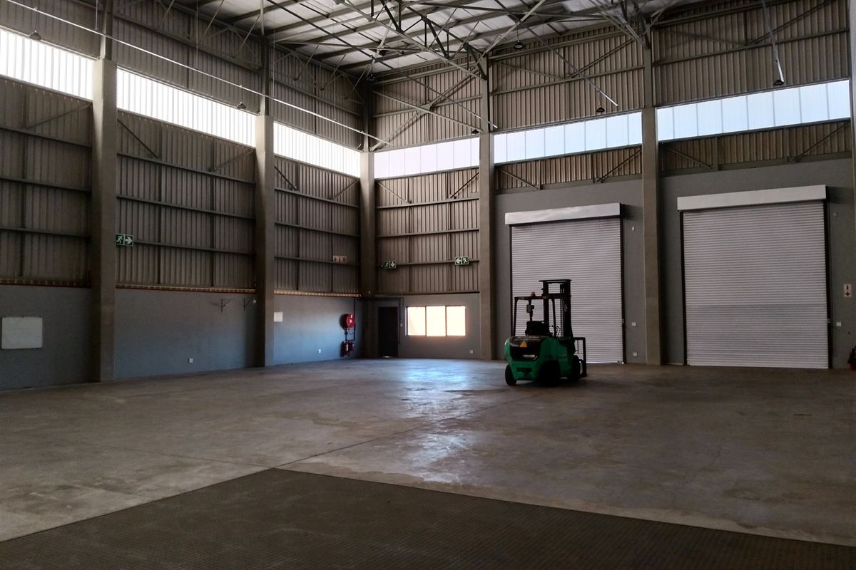 Spacious industrial warehouse featuring high ceilings with exposed steel trusses, concrete flooring, and multiple large roller shutter doors for efficient access.