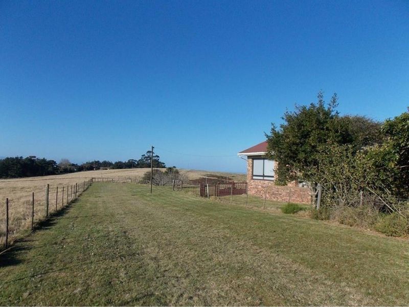 A view of the farm property exterior, showcasing the expansive surrounding fields, open landscape, and the side elevation of the brick farmhouse.