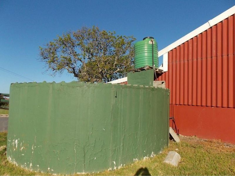 Exterior view of a farm building featuring a large green water storage tank and corrugated metal siding.