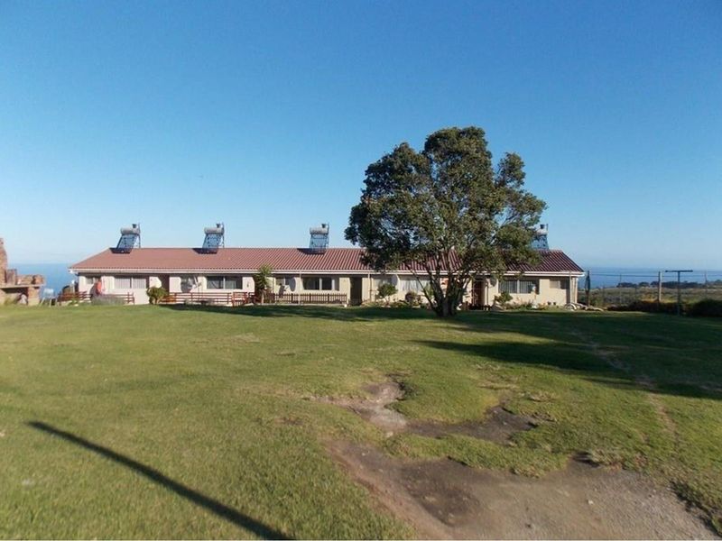 A wide-angle view of the rear exterior of a farm-style residence featuring a tiled roof, solar water heaters, and expansive surrounding lawn.
