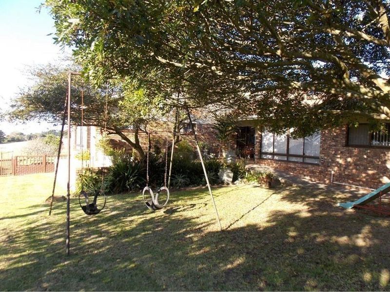 A rear view of the farm property featuring a brick facade, established trees, and a lawn area.