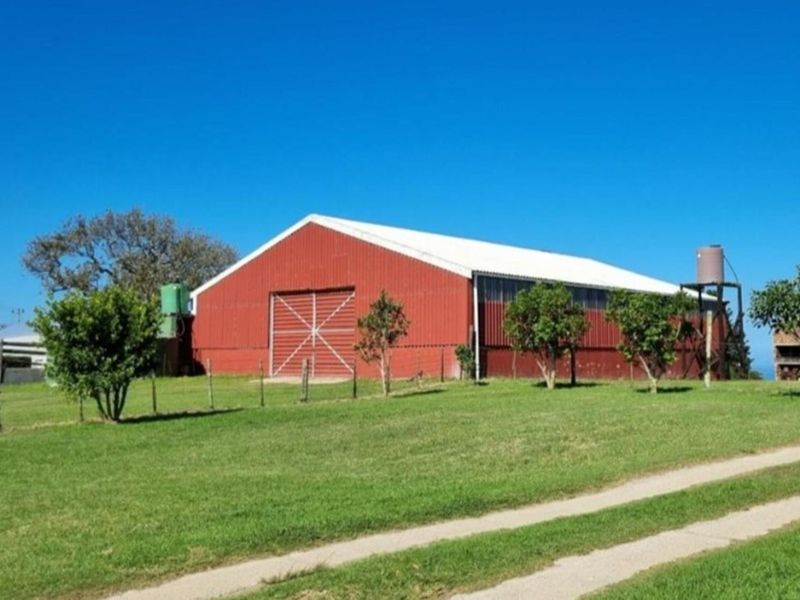 A large red metal farm shed or barn structure situated on a grassy plot with a water tank and gravel access path.