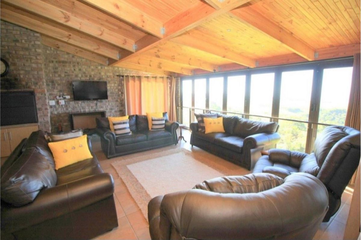 Spacious living room featuring exposed timber beam vaulted ceilings, a rustic brick fireplace, and expansive floor-to-ceiling windows offering panoramic views.