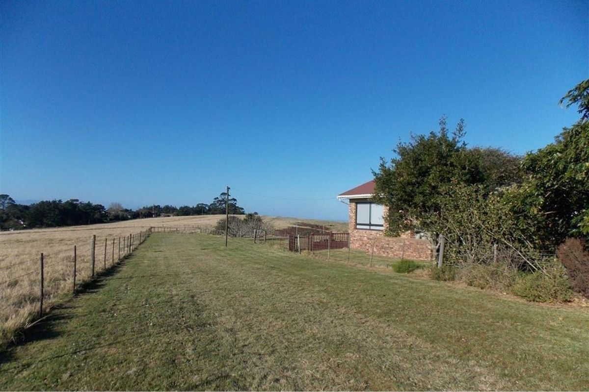 A view of the farm property exterior, showcasing the expansive surrounding fields, open landscape, and the side elevation of the brick farmhouse.
