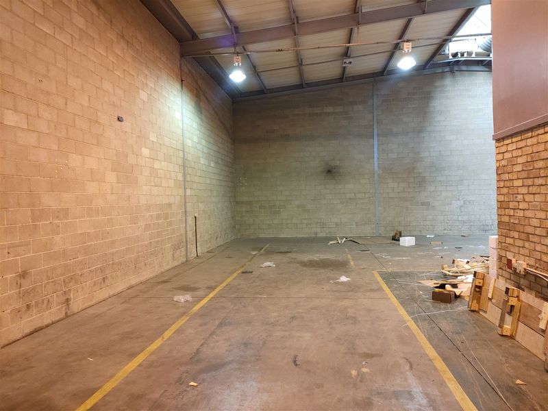 Spacious industrial utility area featuring exposed steel roof trusses, concrete block walls, and durable concrete flooring with industrial lighting.