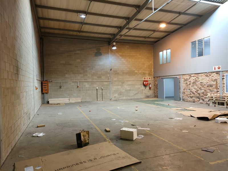 Spacious industrial utility area featuring high ceilings with exposed steel trusses, concrete flooring, and a combination of cinder block and brick wall finishes.