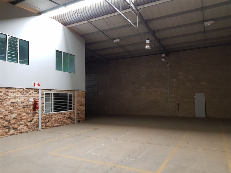 Spacious industrial warehouse unit featuring high ceilings, exposed brick walls, concrete flooring, and integrated office space with large windows.