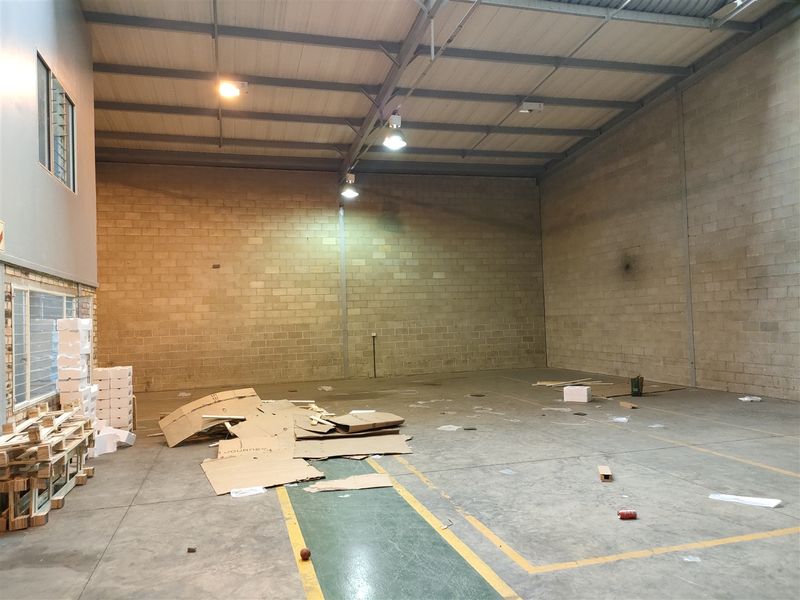 Spacious industrial warehouse unit featuring high ceilings, exposed steel roof structure, concrete block walls, and durable concrete flooring with industrial lighting.