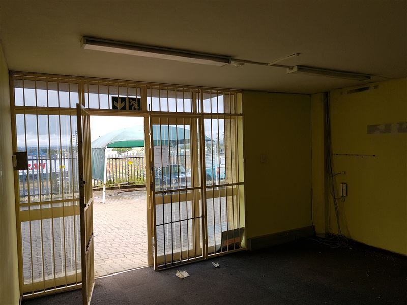 An empty industrial entry space featuring a security gate, fluorescent lighting, and direct access to a paved exterior area.