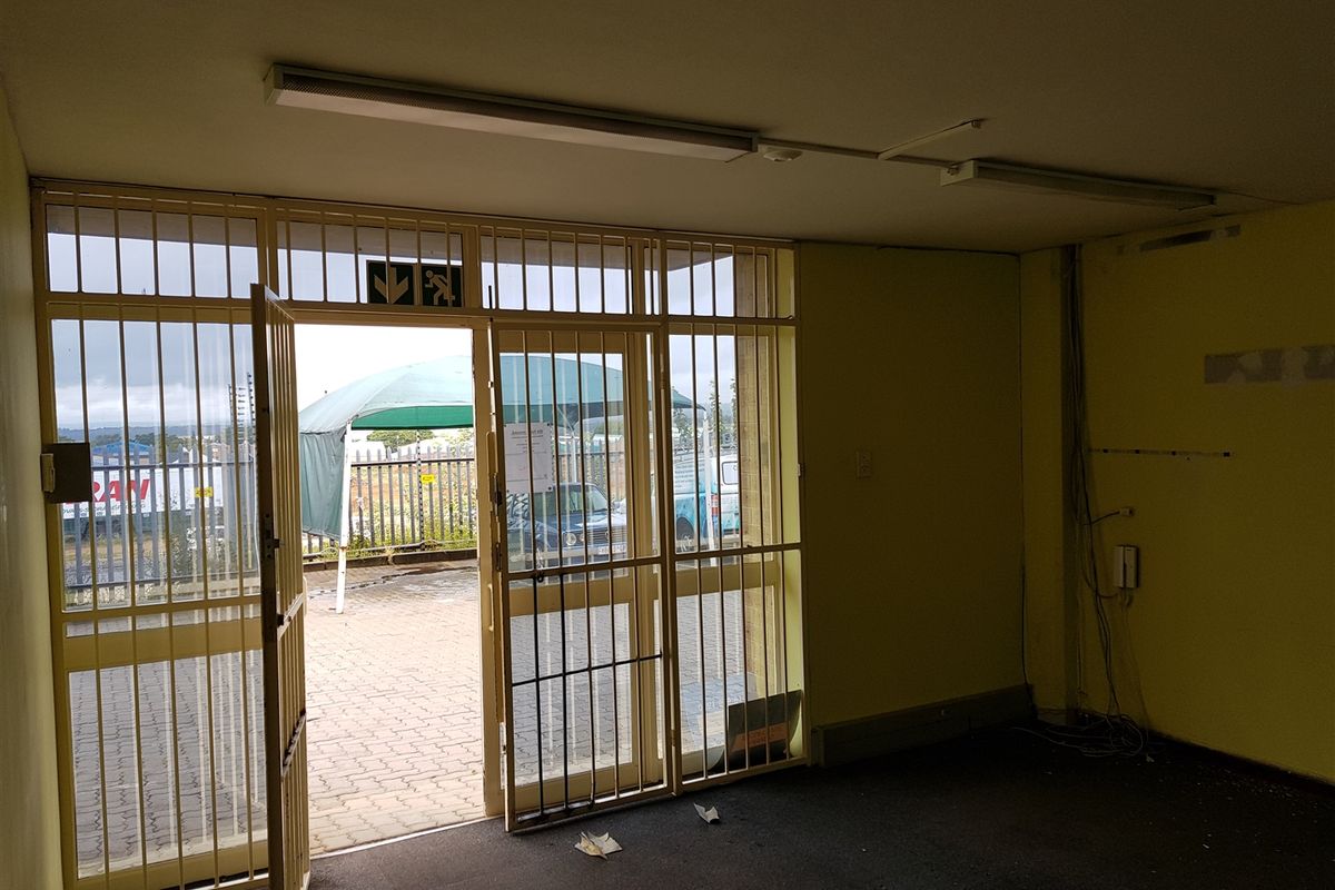 An empty industrial entry space featuring a security gate, fluorescent lighting, and direct access to a paved exterior area.