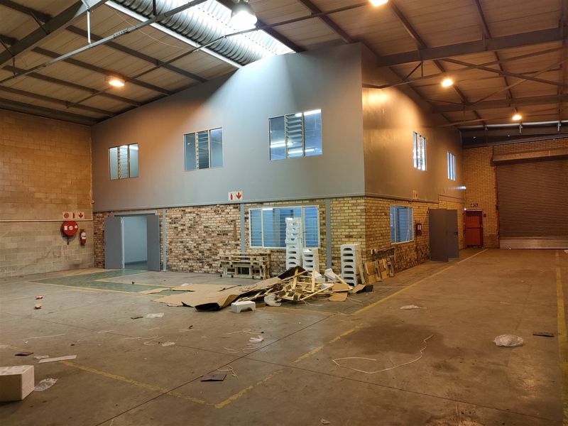 Spacious industrial warehouse unit featuring a mezzanine level, exposed steel roof trusses, concrete flooring, and a large roller shutter door for easy access.