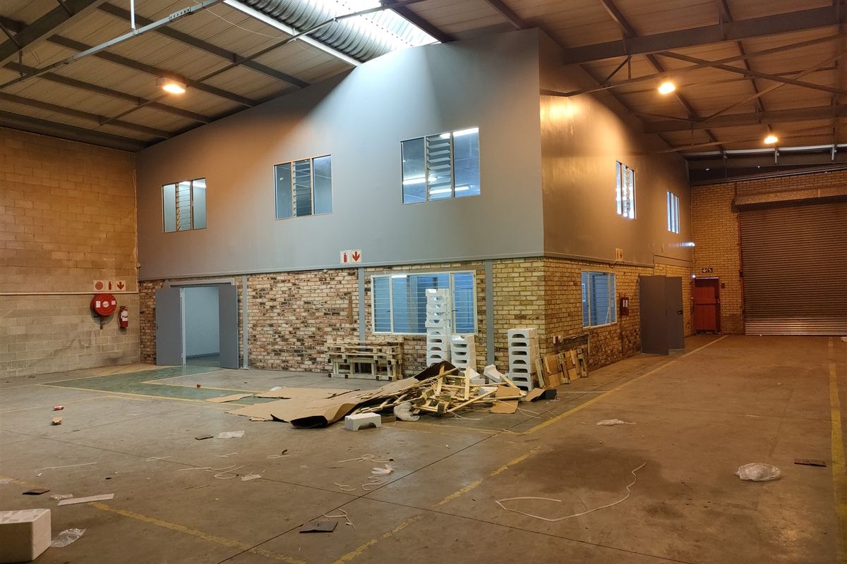 Spacious industrial warehouse unit featuring a mezzanine level, exposed steel roof trusses, concrete flooring, and a large roller shutter door for easy access.