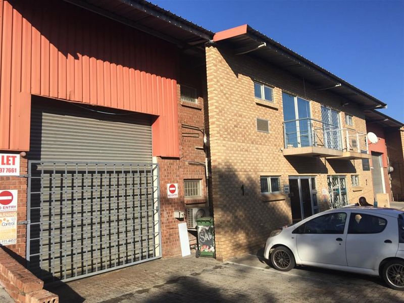 Industrial property exterior featuring a large roller shutter door, brick facade, and an upper-level balcony with metal railings.