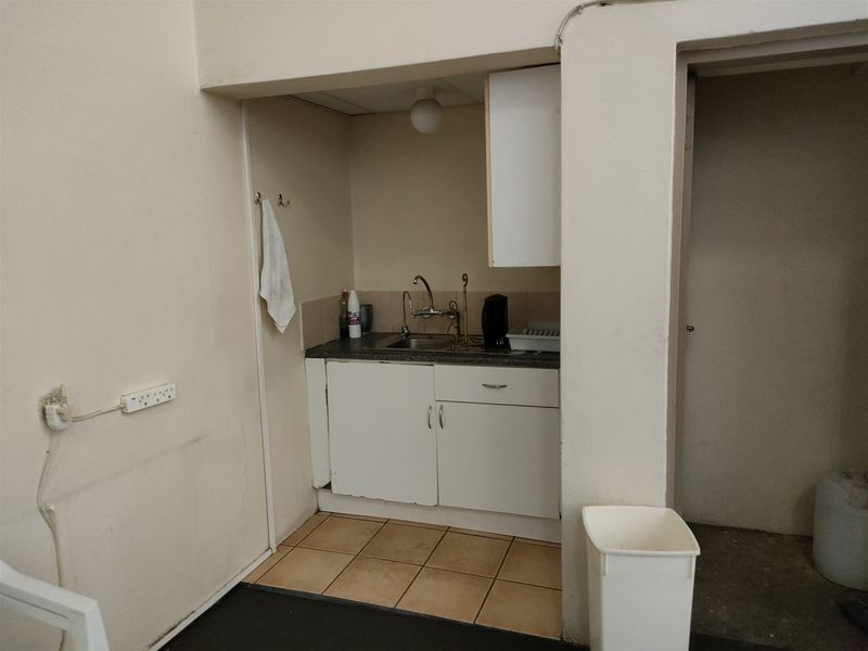 A compact scullery or kitchenette area featuring built-in cabinetry, a stainless steel sink, and tiled flooring, suitable for a small utility or prep space.