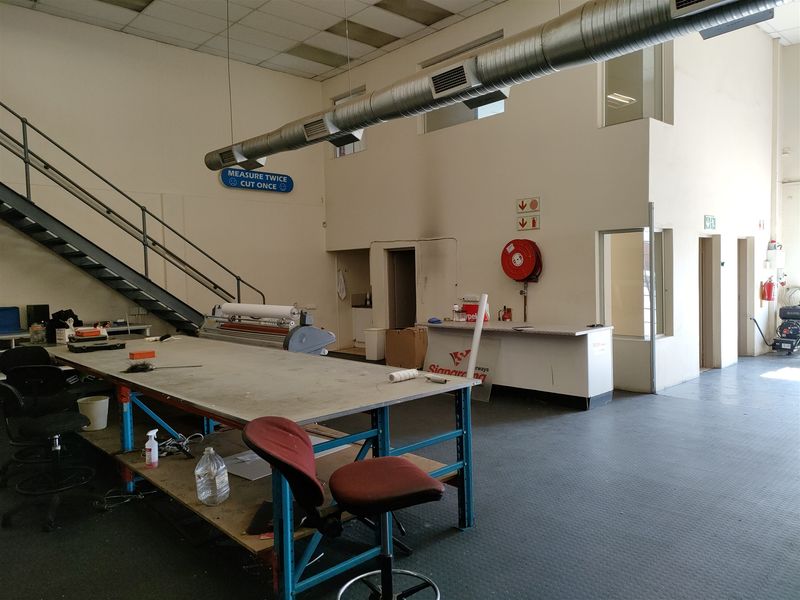 Industrial utility space featuring exposed ventilation ducting, a metal staircase, and functional built-in counter space, suitable for workshop or storage operations.