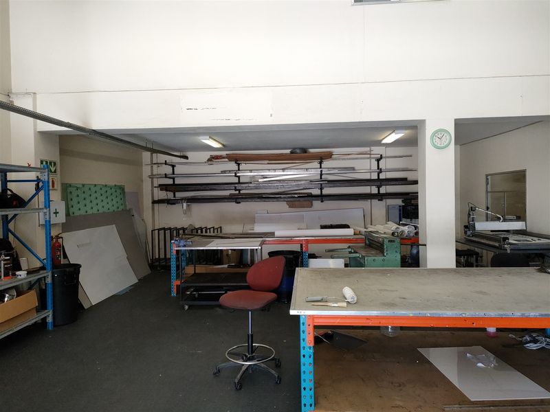 Industrial utility space featuring fixed workbenches, heavy-duty shelving units, and overhead fluorescent lighting, suitable for workshop or storage operations.