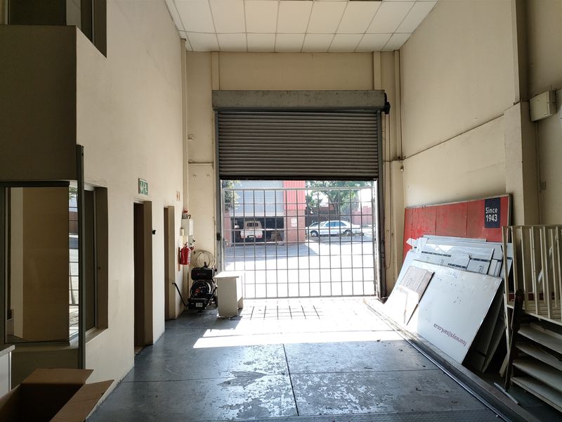 Industrial warehouse or garage space featuring a high roller shutter door, concrete flooring, and a suspended ceiling, suitable for storage or light industrial use.