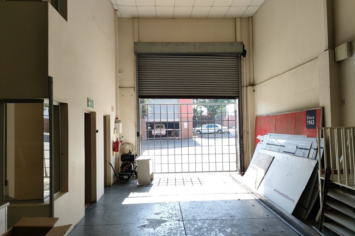 Industrial warehouse or garage space featuring a high roller shutter door, concrete flooring, and a suspended ceiling, suitable for storage or light industrial use.