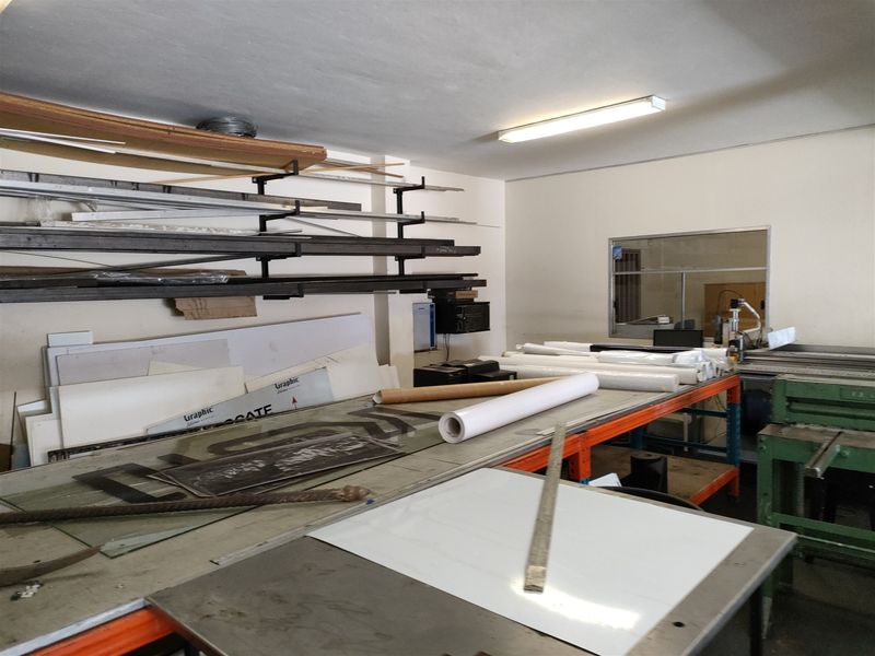 Industrial utility space featuring wall-mounted storage racking, a large workbench, and an internal service window, suitable for workshop or production activities.