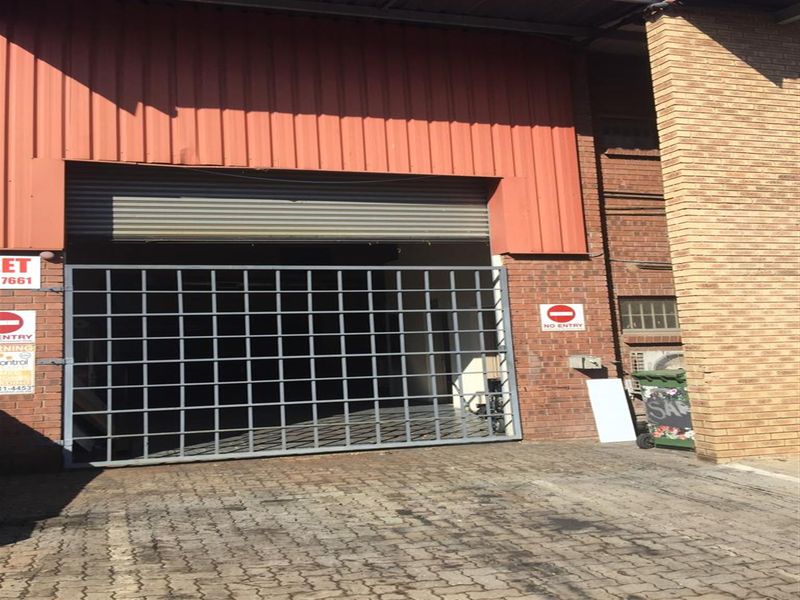 Industrial property exterior featuring a large roller shutter door, metal security gate, and brick facade with paved driveway access.