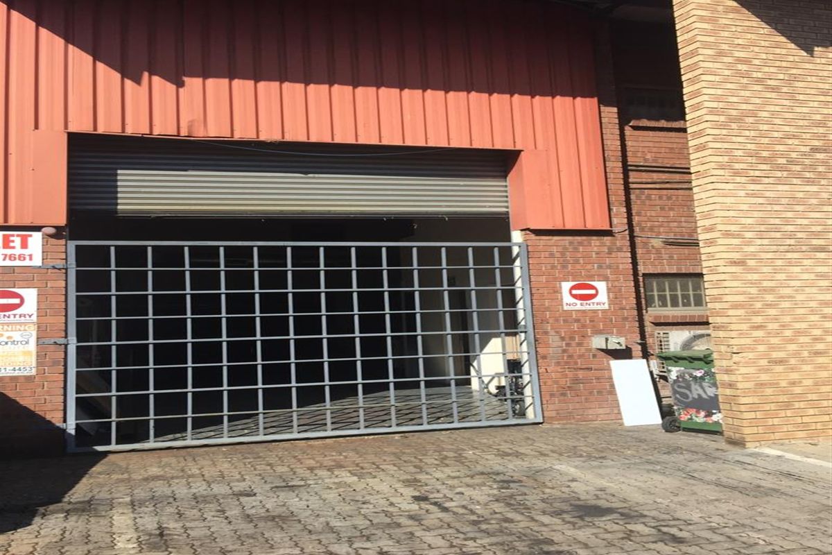 Industrial property exterior featuring a large roller shutter door, metal security gate, and brick facade with paved driveway access.