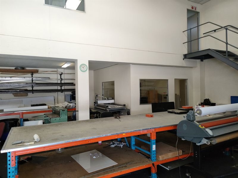 Industrial workspace featuring a mezzanine level, metal staircase, and fixed heavy-duty work benches suitable for manufacturing or production operations.