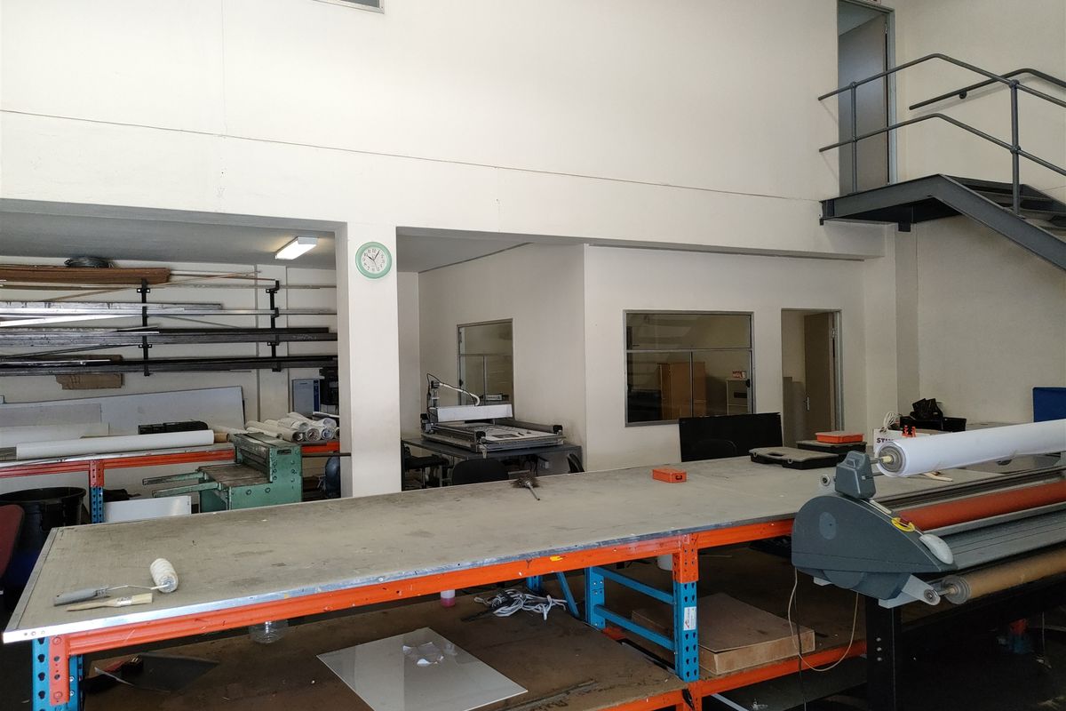 Industrial workspace featuring a mezzanine level, metal staircase, and fixed heavy-duty work benches suitable for manufacturing or production operations.