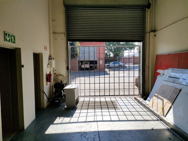 Industrial garage space featuring a large roller shutter door, security gate, and concrete flooring, suitable for storage or workshop use.