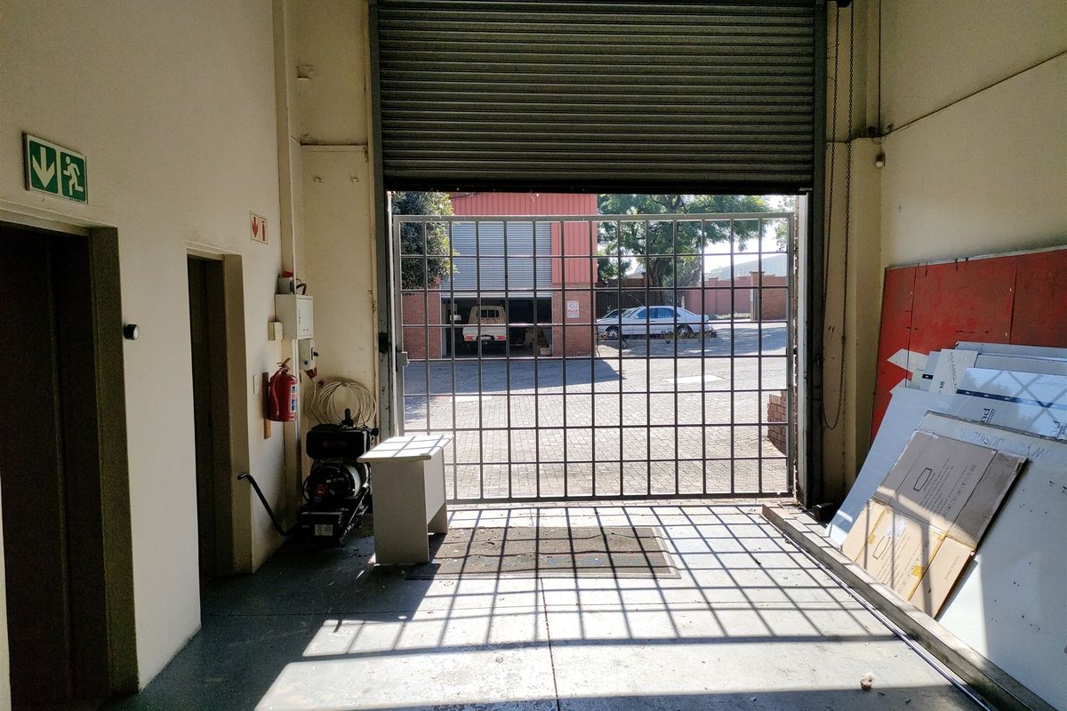Industrial garage space featuring a large roller shutter door, security gate, and concrete flooring, suitable for storage or workshop use.