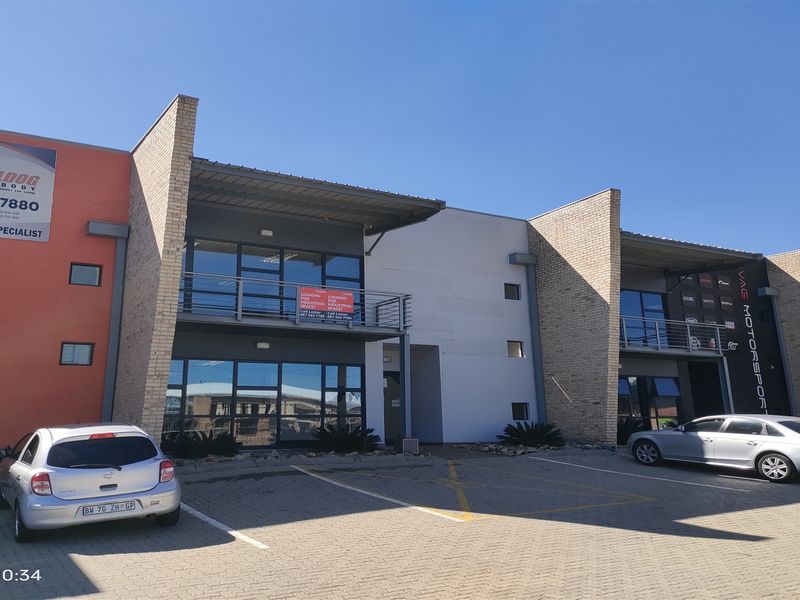 Front elevation of a modern industrial complex featuring brick and rendered facades, aluminum windows, and a paved parking area.