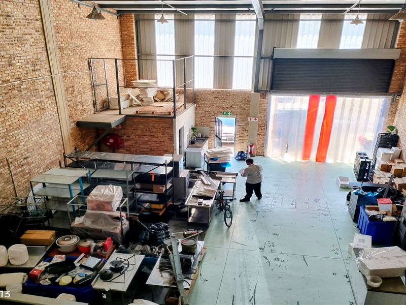 Spacious industrial warehouse unit featuring exposed brick walls, a mezzanine level, high ceilings, and a large roller shutter door for easy access.