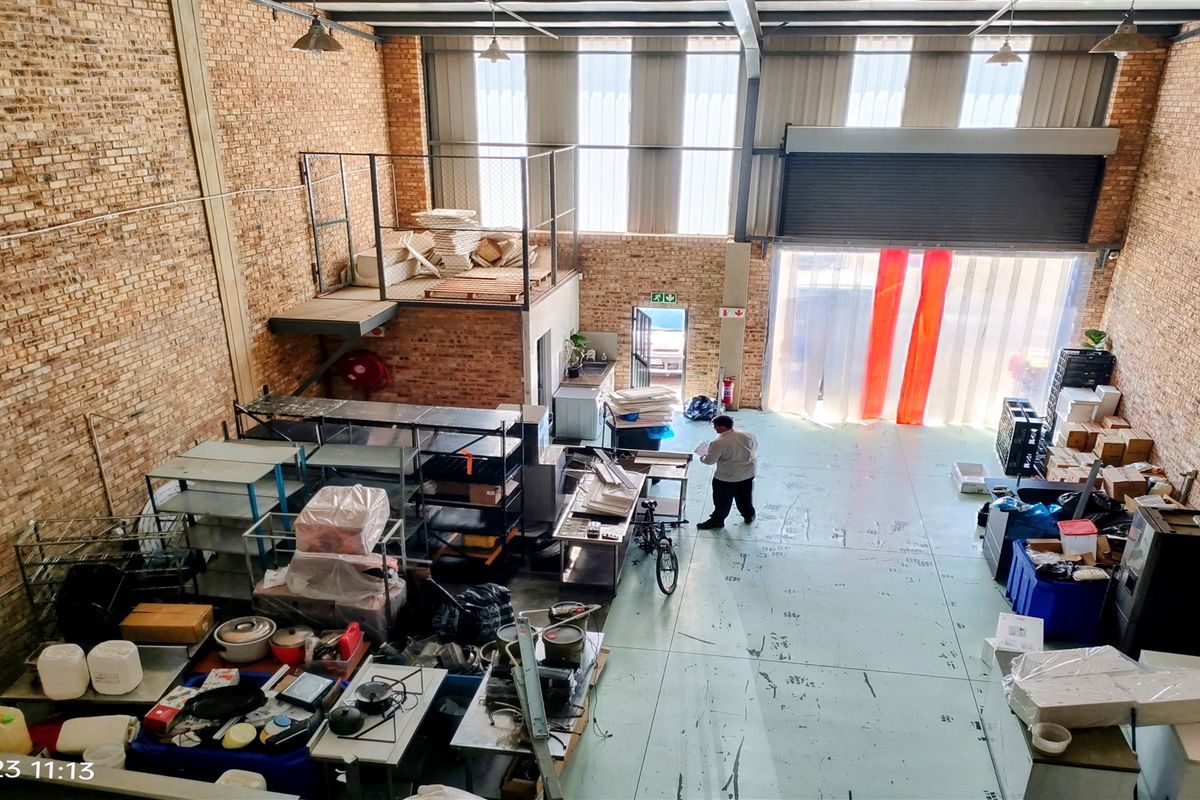 Spacious industrial warehouse unit featuring exposed brick walls, a mezzanine level, high ceilings, and a large roller shutter door for easy access.