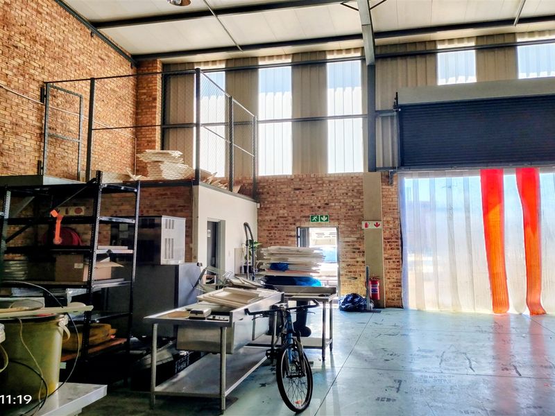 Industrial warehouse space featuring exposed brick walls, a mezzanine level, concrete flooring, and a large roller shutter door for easy access.