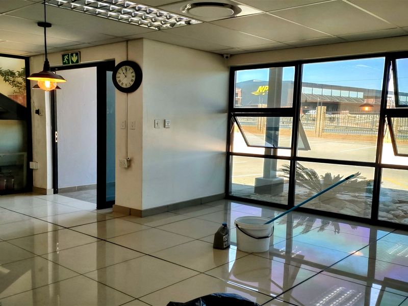 A bright, open-plan office space featuring large windows, tiled flooring, and a modern staircase, suitable for a professional industrial or commercial workspace.