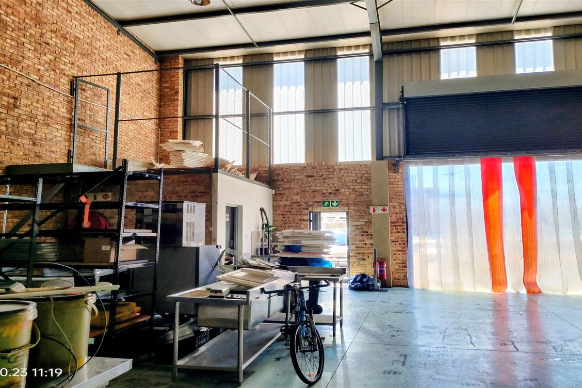 Industrial warehouse space featuring exposed brick walls, a mezzanine level, concrete flooring, and a large roller shutter door for easy access.